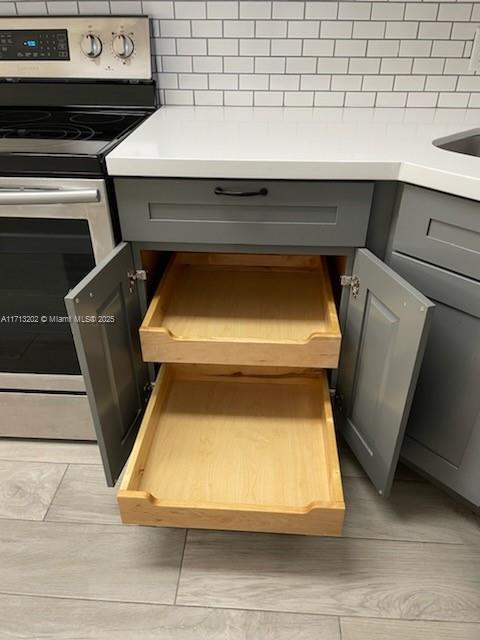 interior details featuring gray cabinets, stainless steel electric range oven, and tasteful backsplash