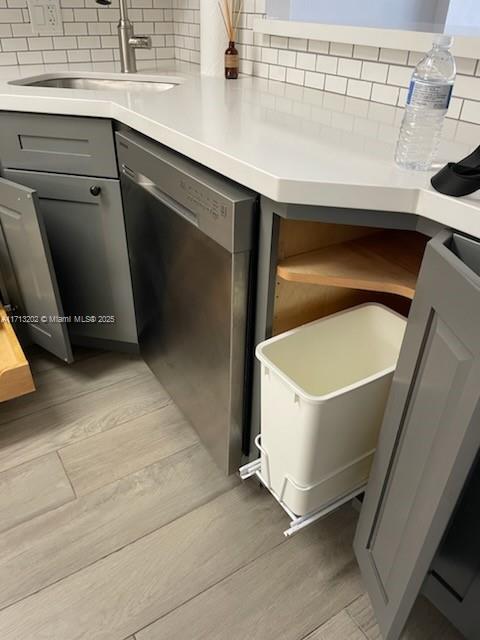 interior details featuring gray cabinetry, backsplash, sink, light hardwood / wood-style flooring, and stainless steel dishwasher