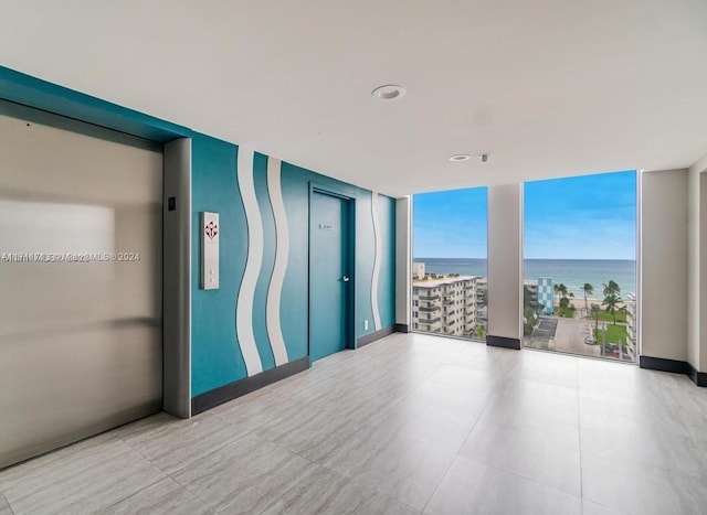 spare room featuring elevator, a water view, and a wall of windows