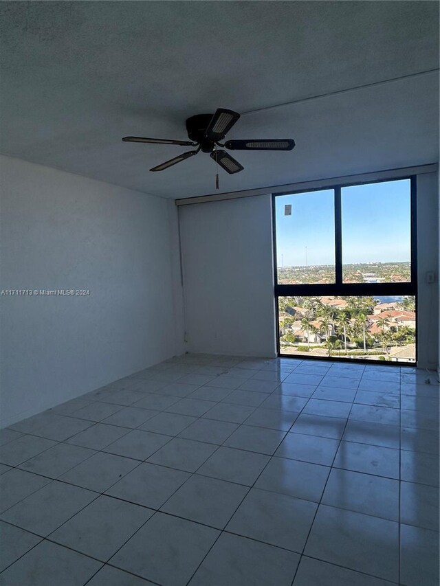 tiled empty room featuring ceiling fan, floor to ceiling windows, and a textured ceiling