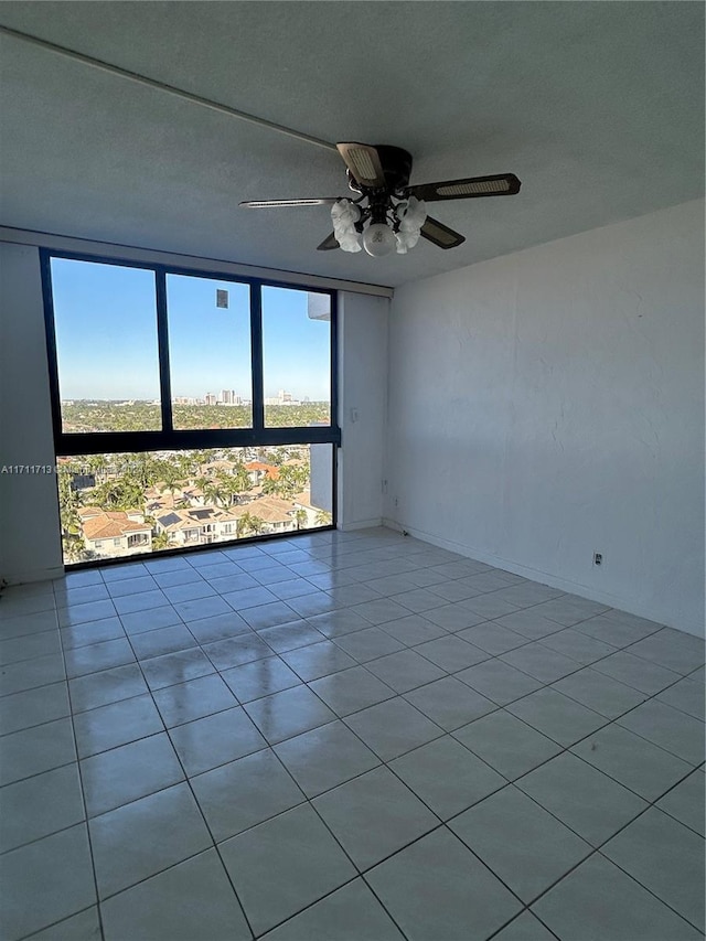 empty room featuring ceiling fan, expansive windows, and light tile patterned floors