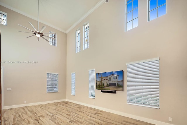 unfurnished living room with ceiling fan, light hardwood / wood-style flooring, crown molding, plenty of natural light, and a towering ceiling