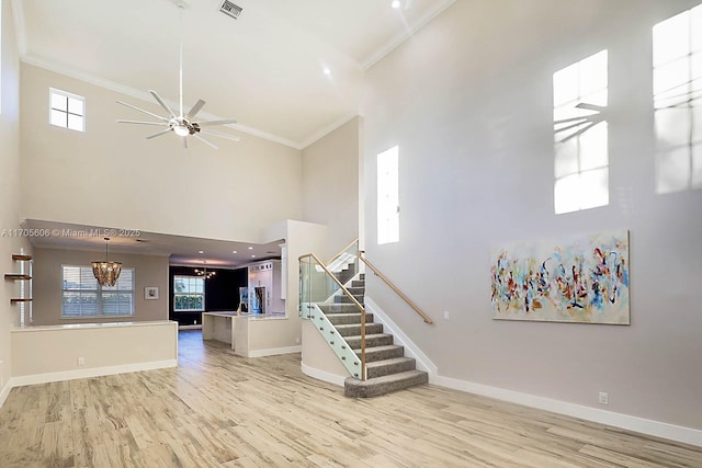 staircase featuring crown molding, a towering ceiling, wood-type flooring, and ceiling fan with notable chandelier