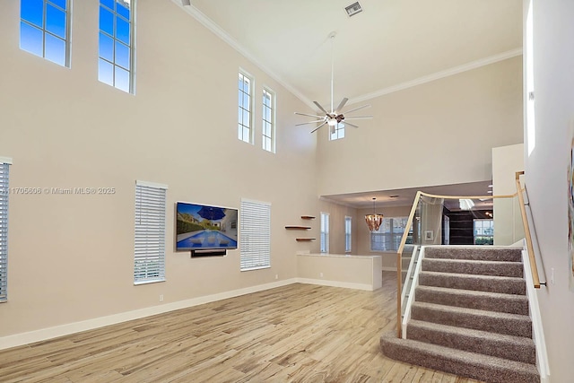 interior space featuring hardwood / wood-style floors, ceiling fan with notable chandelier, ornamental molding, and a high ceiling