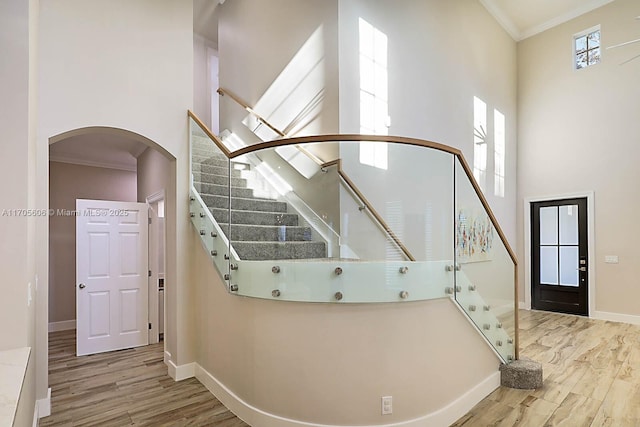 stairway with a towering ceiling, hardwood / wood-style flooring, and ornamental molding