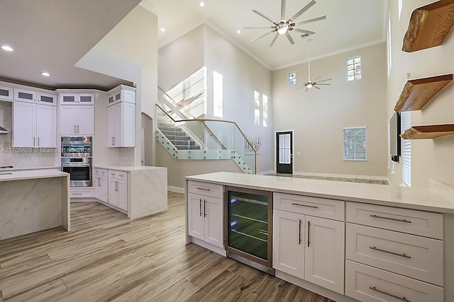 kitchen with backsplash, crown molding, wine cooler, light wood-type flooring, and white cabinetry