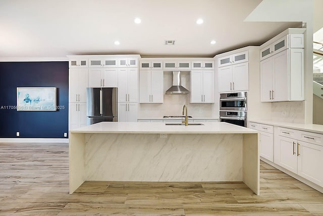 kitchen featuring sink, wall chimney exhaust hood, stainless steel appliances, an island with sink, and decorative backsplash