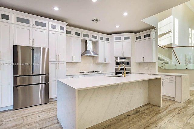 kitchen featuring white cabinetry, sink, wall chimney range hood, an island with sink, and appliances with stainless steel finishes