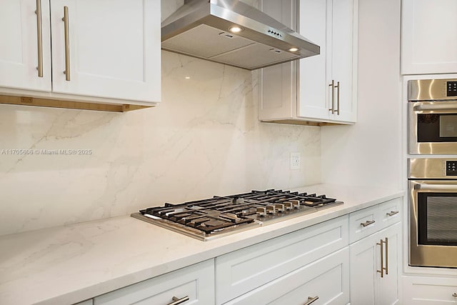 kitchen with white cabinetry, light stone countertops, stainless steel appliances, decorative backsplash, and exhaust hood