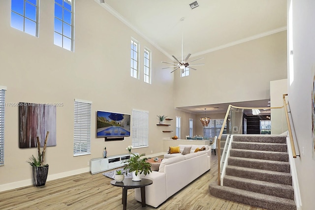 living room with a high ceiling, light hardwood / wood-style floors, ceiling fan with notable chandelier, and ornamental molding