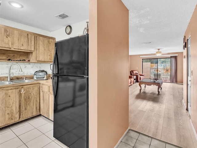 kitchen with light tile patterned floors, light countertops, a ceiling fan, freestanding refrigerator, and a sink