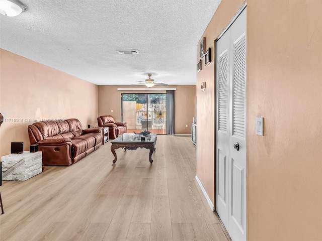 living area with a ceiling fan, light wood-style flooring, visible vents, and a textured ceiling