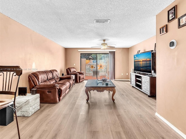 living room featuring baseboards, a textured ceiling, visible vents, and light wood-style floors