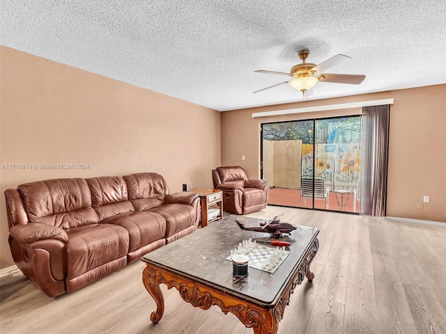 living room featuring baseboards, ceiling fan, light wood-style flooring, and a textured ceiling