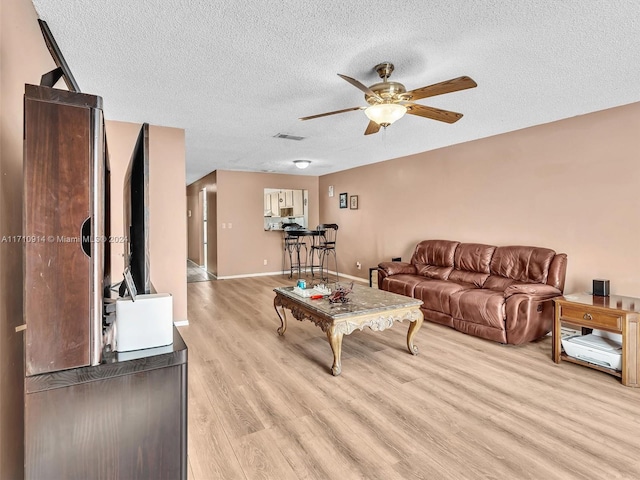 living area with a textured ceiling, visible vents, baseboards, a ceiling fan, and light wood finished floors