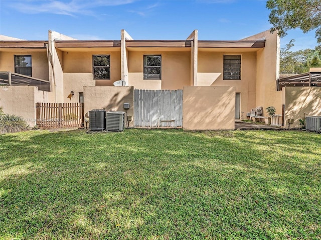 rear view of property with fence, central AC unit, a lawn, and stucco siding