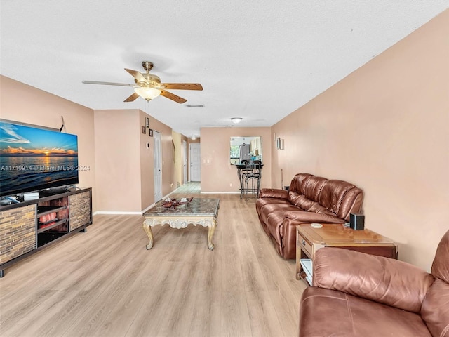 living room featuring a ceiling fan, baseboards, light wood-style flooring, and a textured ceiling