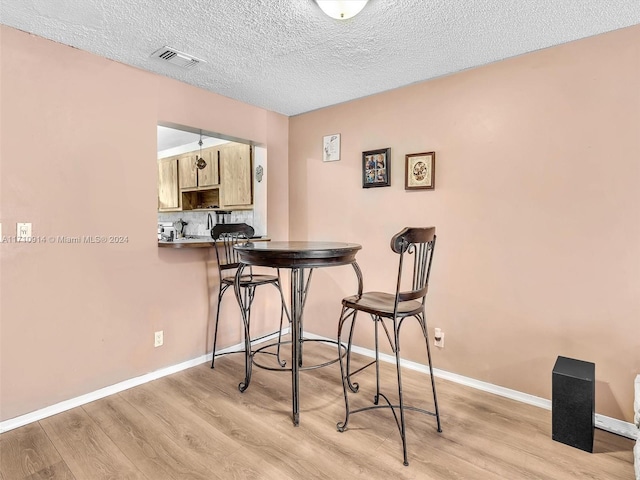 dining room featuring a textured ceiling, light wood-type flooring, visible vents, and baseboards