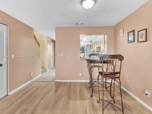 dining room featuring a textured ceiling, light wood-style flooring, visible vents, baseboards, and stairway