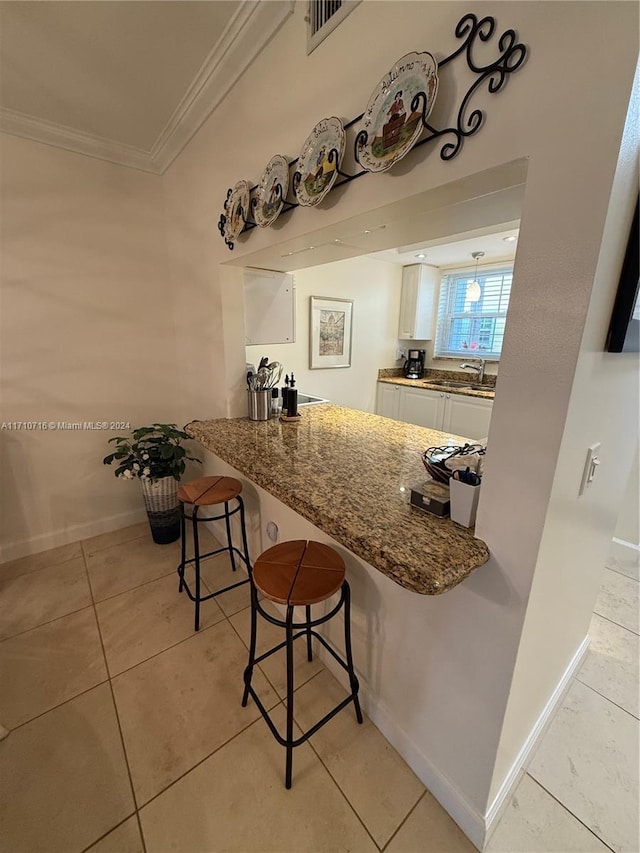 kitchen with sink, light tile patterned floors, ornamental molding, a kitchen bar, and white cabinetry