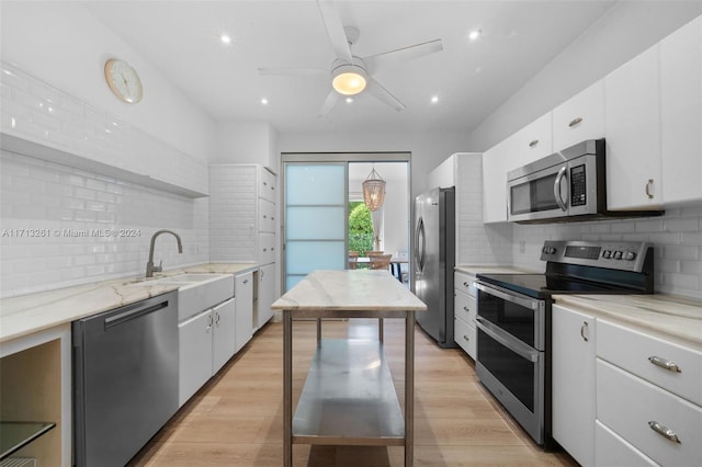 kitchen with appliances with stainless steel finishes, light wood-type flooring, backsplash, sink, and white cabinets