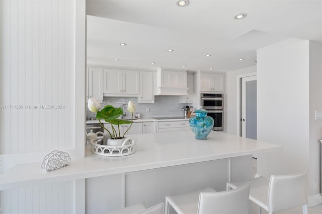 kitchen with a kitchen bar, stainless steel double oven, backsplash, and white cabinetry