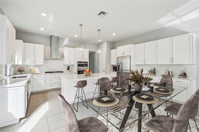 kitchen featuring a center island, sink, wall chimney exhaust hood, decorative backsplash, and appliances with stainless steel finishes