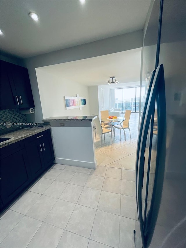 kitchen featuring kitchen peninsula, backsplash, sink, blue cabinetry, and light tile patterned floors