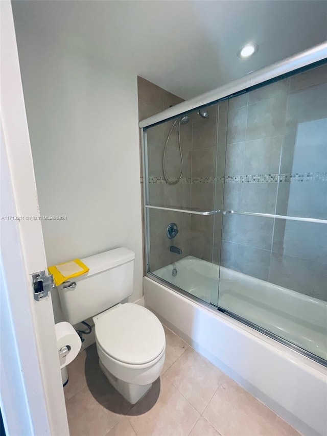 bathroom featuring tile patterned flooring, bath / shower combo with glass door, and toilet