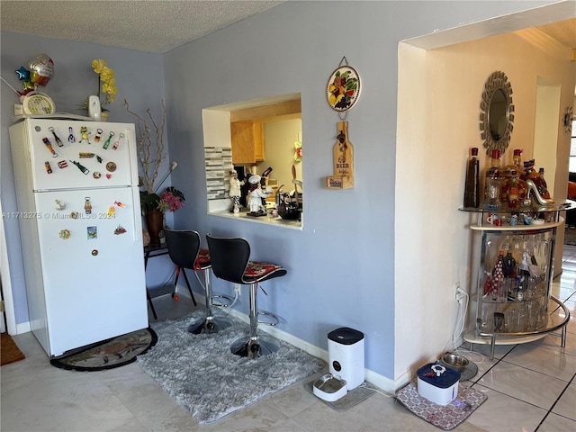 kitchen with white fridge, light tile patterned flooring, and a textured ceiling