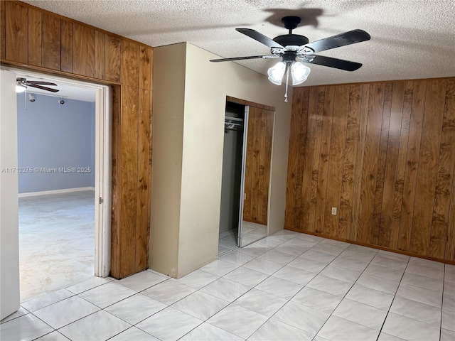 unfurnished bedroom featuring a closet, wooden walls, a textured ceiling, and a ceiling fan