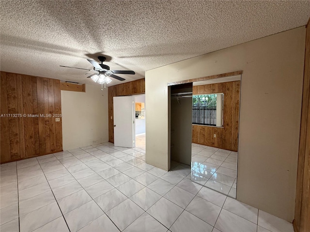empty room with a textured ceiling, wood walls, ceiling fan, and light tile patterned floors