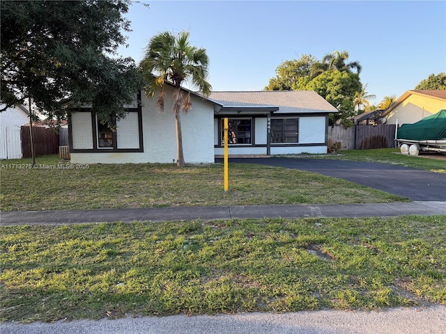 ranch-style home featuring aphalt driveway, a front yard, and fence