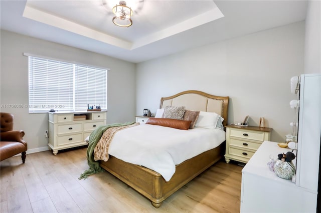 bedroom with light hardwood / wood-style floors and a tray ceiling