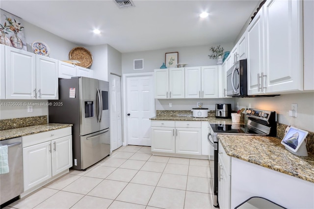 kitchen with light tile patterned floors, appliances with stainless steel finishes, white cabinetry, and light stone counters