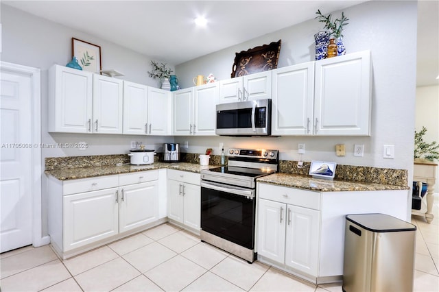 kitchen featuring light tile patterned flooring, appliances with stainless steel finishes, white cabinets, and dark stone counters