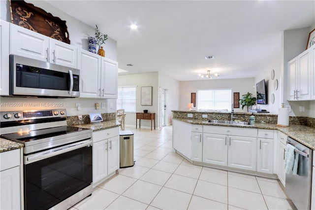 kitchen featuring kitchen peninsula, appliances with stainless steel finishes, dark stone counters, white cabinets, and sink