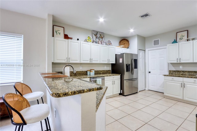 kitchen with white cabinetry, kitchen peninsula, stainless steel appliances, and dark stone counters