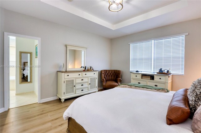 bedroom with ensuite bathroom, light hardwood / wood-style floors, and a raised ceiling