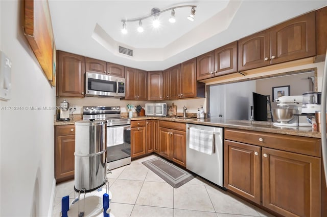 kitchen featuring light stone countertops, appliances with stainless steel finishes, a tray ceiling, sink, and light tile patterned flooring