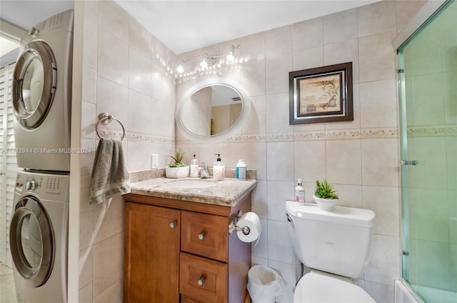 full bathroom with bath / shower combo with glass door, stacked washer / drying machine, toilet, vanity, and tile walls