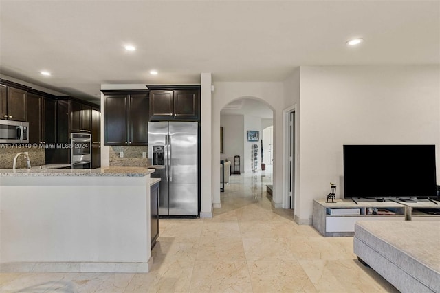 kitchen with appliances with stainless steel finishes, dark brown cabinetry, tasteful backsplash, and light stone counters