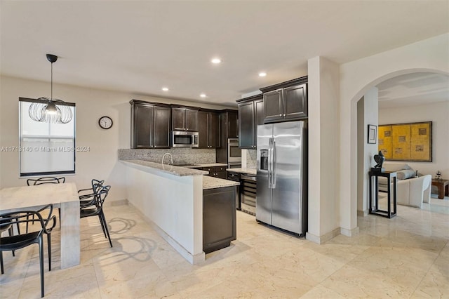 kitchen featuring kitchen peninsula, decorative backsplash, light stone counters, stainless steel appliances, and hanging light fixtures