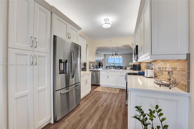 kitchen with pendant lighting, white cabinets, kitchen peninsula, appliances with stainless steel finishes, and wood-type flooring