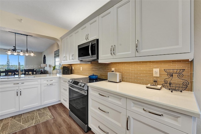 kitchen with backsplash, decorative light fixtures, white cabinets, and stainless steel appliances