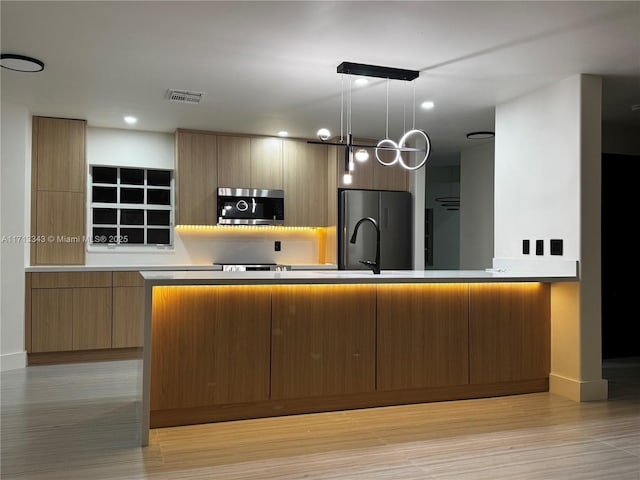 kitchen featuring a center island with sink, stainless steel appliances, hanging light fixtures, and light hardwood / wood-style flooring