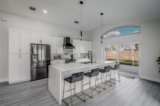 kitchen featuring appliances with stainless steel finishes, wall chimney exhaust hood, a kitchen island with sink, sink, and white cabinetry