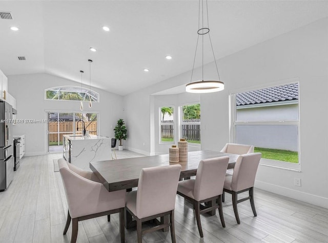 dining room with sink, light hardwood / wood-style floors, and vaulted ceiling