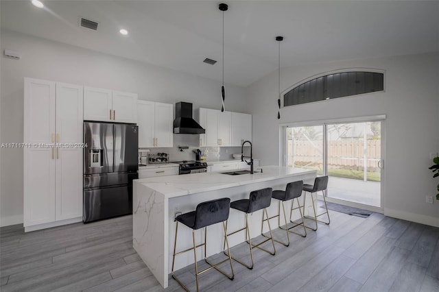 kitchen with white cabinetry, sink, wall chimney exhaust hood, stainless steel fridge with ice dispenser, and a kitchen island with sink