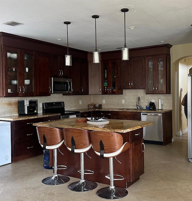 kitchen with light stone countertops, appliances with stainless steel finishes, a center island, and backsplash